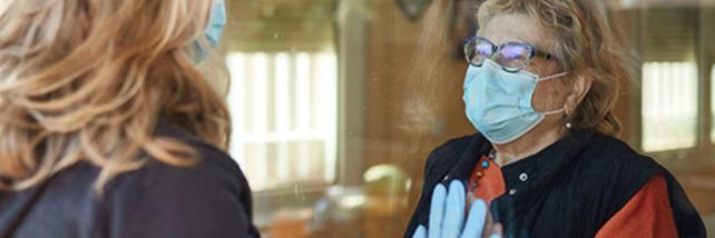 Elderly woman and family member looking at each other through window